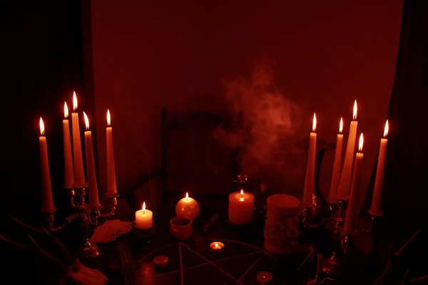 in a dark room on a round esoteric table candles burn, smoke, animal skulls lie, a pentagram is drawn, a red heart model, candles, a concept of magic, witchcraft