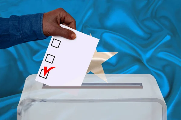 男性の有権者は ソマリアの国旗 州の選挙の概念 国民投票の背景にある透明な投票箱に投票を落とします — ストック写真