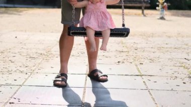 Adam salıncakta sallanan küçük bir kızı sallıyor, elbise giymiş bir bebek ve panama evde yürüyor, mutlu bir çocukluk konsepti, çocuk oyunları, alfa kuşağı.