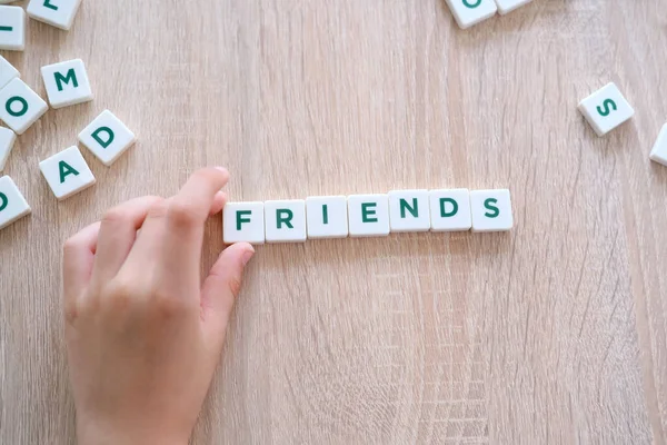 children make up the word friends from letters on a wooden table, the concept of the beginning of the school year, homework, lessons, back to school