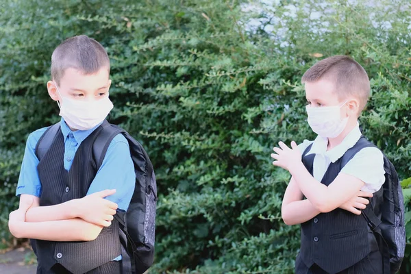 two boys, schoolchildren in black clothes with their faces covered by a medical mask quarreled, turned away, the concept of a quarrel and reconciliation of friends, back to school