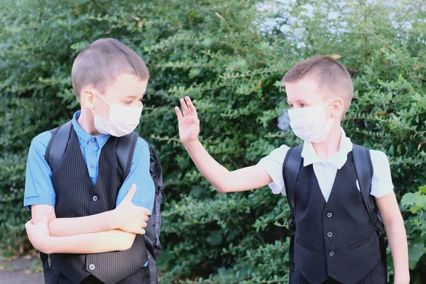 two boys, schoolchildren in black clothes with their faces covered by a medical mask quarreled, turned away, the concept of a quarrel and reconciliation of friends, back to school