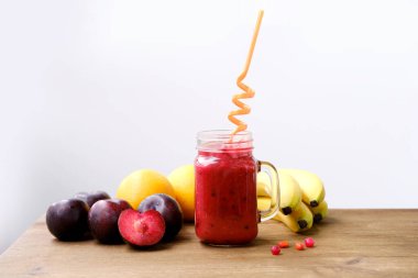 Mason kavanozu kupası, elinde meyve suyu, renkli bir tüp, masada meyveler, çiğ yiyecek konsepti, sağlıklı canlandırıcı içecekler, vitamin diyeti, kilo kaybı.