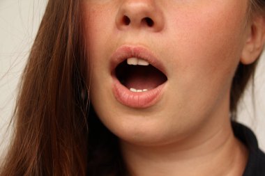 Şarkı söylemek. Yakın plan kadın ağzı, iyi korunmuş yanak derisi. Kozmetoloji, tıp, diş hekimliği, ağız bakımı, duygular ve yüz ifadesi kavramı.