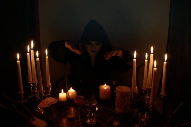 Dişi falcı karanlık bir odada, mumlar pentagramla yuvarlak bir masada yanıyor, hayvan kafatasları yalan söylüyor, sihir kavramı, cadılık kavramı...