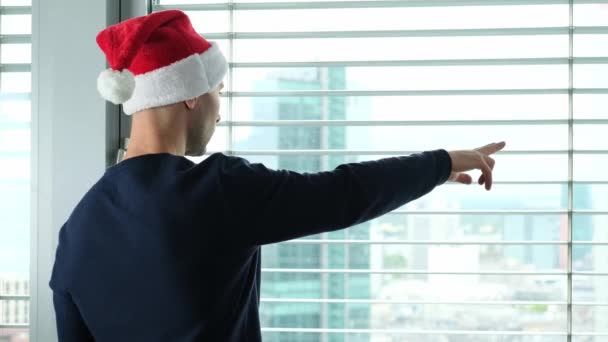头戴圣诞礼帽的年轻人站在窗前 在窗后看得见欧洲的大城市 他们的旅游观念 新年庆祝活动 西尔维斯节 等待节日 圣诞节销售 — 图库视频影像