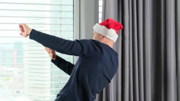 身穿圣爪帽的年轻人欢快地在窗前跳舞 旅游的理念 旅游的理念 新年的庆祝活动 等待节日的到来 圣诞节的销售 — 图库视频影像