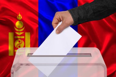 Erkek seçmen, Moğolistan bayrağı, devlet seçimleri konsepti ve referandumun arka planında şeffaf bir sandık içinde oy kullanıyor.