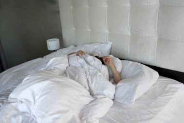 Genç bir kadın bir otelde bir yatakta uyuyor, güzel beyaz yatak, bir sürü yastık, iş gezisi konsepti, seyahat, turizm, sağlıklı uyku, uykusuzluk sorunu