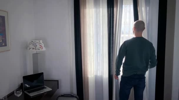 Молодой Человек Стоит Перед Окном Открывает Занавески Смотрит Улицу Концепцию — стоковое видео