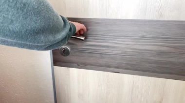 Gri kazaklı ve kot pantolonlu genç adam ofiste, evde, otel odasında, iş seyahati, turizm, işyeri konsepti, açık kapı açıyor.