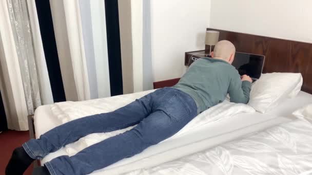 Młody Łysy Mężczyzna Szarym Swetrze Dżinsach Leży Łóżku Pokoju Hotelowym — Wideo stockowe