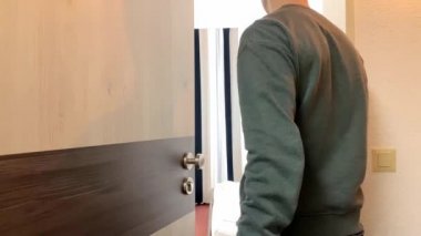 Gri kazaklı ve kot pantolonlu genç adam ofiste, evde, otel odasında bir ışık kapısı açıyor, içeri giriyor, iş seyahati, turizm, işyeri konsepti, evde kalıyor.
