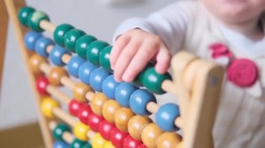 Çocuk, küçük parmaklarla bebek sayımı, ahşap çocuk abaküsünde renkli zarlar, matematik, hesaplamalar, bir çocuğun zihinsel gelişimi.