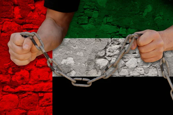 male hands breaking the iron chain, symbol of bondage, protest against background of state flag of United Arab Emirates, concept of political repression, tyranny, arrest, crime, civil rights, freedom