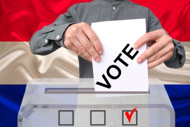 Erkek seçmen, Hollanda bayrağının arka planına, devlet seçimleri konseptine, referanduma karşı şeffaf bir sandık içinde oy kullanıyor.