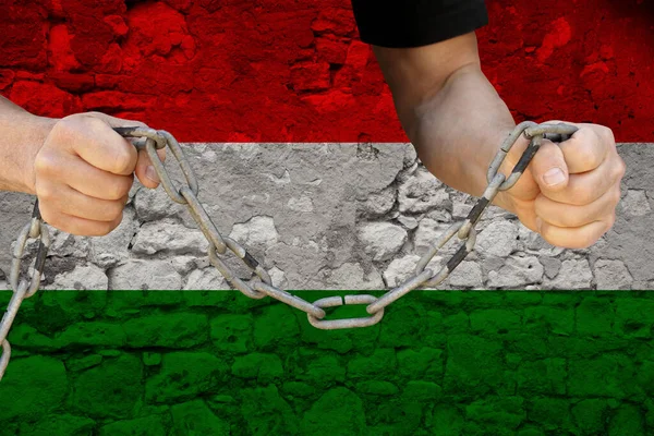 male hands breaking the iron chain, symbol of bondage, protest against the background of the state flag of Hungary, the concept of political repression, tyranny, arrest, crime, civil rights, freedom