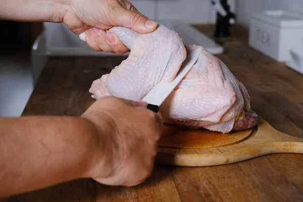 woman processes chicken, prepares food in the kitchen, cuts poultry meat into pieces with a porcelain knife, concept of traditional cuisine