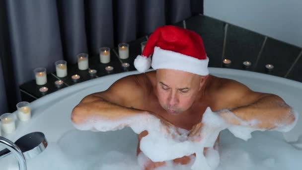 头戴圣诞礼帽的成年人坐在一个大的圆形浴缸里 玩泡沫游戏 模仿冬天的雪 圣诞观念 新年庆祝 个人卫生 — 图库视频影像