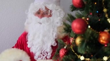 Kırmızı takım elbiseli Noel Baba masaya oturur, ağaç toplar, çelenkler, noel konsepti, yeni yıl kutlaması, tatil satışları ve indirimlerle süslenir.
