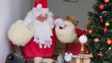 Kırmızı takım elbiseli yetişkin Noel Baba masaya oturur, Noel ağacı toplar, çelenkler, Noel konsepti, yeni yıl kutlaması, tatil satışları ve indirimlerle süslenir.