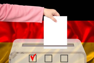 Kadın seçmen, Almanya bayrağı, devlet seçimleri ve referandumun arka planına karşı şeffaf bir oy sandığında oy kullanıyor.