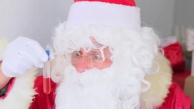 Beyaz sakallı Noel Baba laboratuvarda kan örneği inceler, DNA testi yapar, COVID-19 aşısına karşı aşı inceler, Noel konsepti, hediyeleri bekler, yeni yılı kutlar.