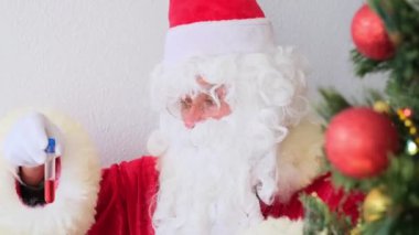 Beyaz sakallı Noel Baba laboratuvarda kan örneği inceler, DNA testi yapar, COVID-19 aşısına karşı aşı inceler, Noel konsepti, hediyeleri bekler, yeni yılı kutlar.