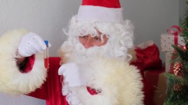 Beyaz sakallı Noel Baba laboratuvarda kan örneği inceler, DNA testi yapar, COVID-19 aşısına karşı aşı inceler, Noel konsepti, hediyeleri bekler, yeni yılı kutlar.