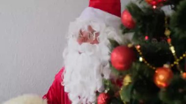 Kırmızı takım elbiseli, beyaz sakallı Noel Baba ağacın yanında oturuyor, tüyle, noel konseptiyle mektup yazıyor, hediyeleri bekliyor, yeni yılı kutluyor, tatil satışları, Nicholas Günü.