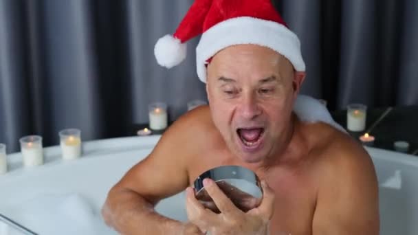 头戴圣诞礼帽的成年人坐在一个巨大的圆形浴池里 情绪激昂 有圣诞节的观念 有新年庆祝活动 有卫生习惯 — 图库视频影像