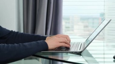 Genç adam, modern bir Avrupa şehrinin penceresinin önündeki bir ofiste dizüstü bilgisayarın arkasında çalışıyor. İş fikirleri kavramı, işyeri.