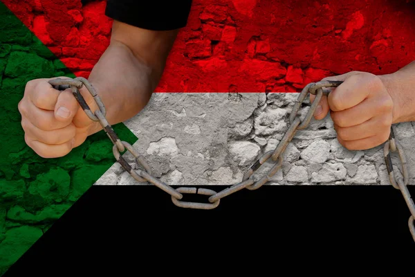 male hands breaking the iron chain, symbol of bondage, protest against the background of the national flag of Sudan, the concept of political repression, tyranny, arrest, crime