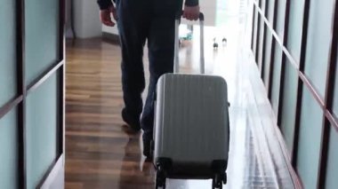 Gri kazaklı ve kot pantolonlu genç adam otel odasına bavuluyla girdi, pencerenin önünde durdu, iş seyahati, turizm kavramı...