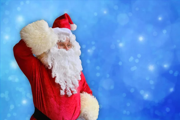 adult santa claus with a white beard on a beautiful blue background looking away, christmas concept, waiting for gifts, sales and discounts, festive mood