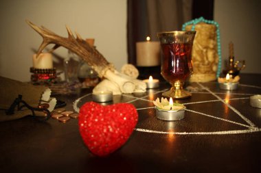 in a dark room candles are burning on a round esoteric table, animal skulls are lying, a pentagram is drawn, a model of a red heart, candles, a concept of magic, witchcraft clipart