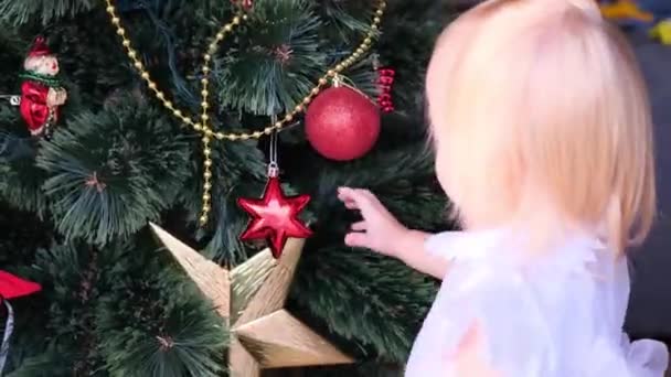 Ребенок Маленькая Блондинка Белом Платье Играет Новогодними Украшениями Рассматривает Рождественские — стоковое видео