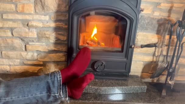 男は熱い燃える暖炉の近くにあります 足は火に赤い靴下で伸ばし クリスマスの概念 冬のリラクゼーション — ストック動画