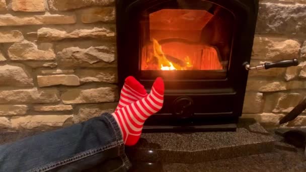 男人躺在炽热的壁炉边 穿着红袜的腿伸向火堆 有圣诞节的念头 还有寒假 — 图库视频影像