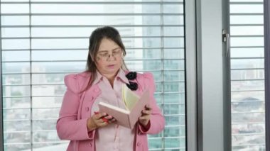 Modern bir şehir ofisinde pembe elbiseli yetişkin bir kadın, müdür, not defterine not alıyor, iş fikirleri kavramı, iş yeri, çalışma saatlerinin dağıtımı