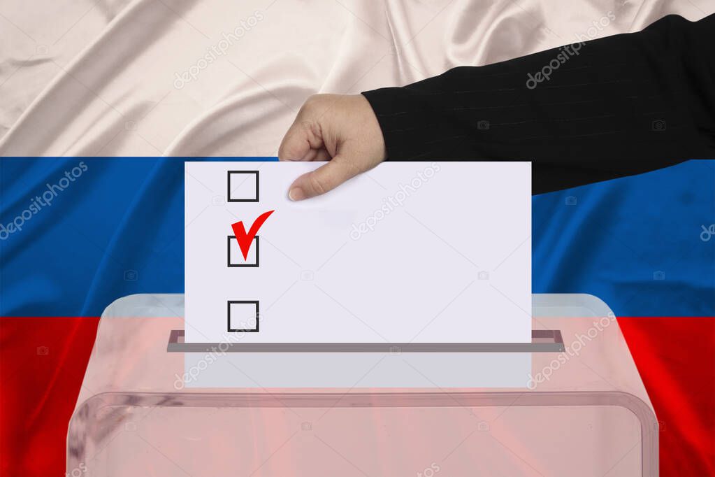 woman voter lowers the ballot in a transparent ballot box on the background of the national flag of Russia concept of state elections, referendum