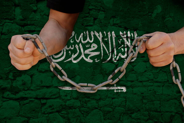 male hands breaking iron chain, symbol of tyranny, protest against of national flag kingdom of saudi arabia with Arabic inscription There is no God but Allah no prophet except Muhammad
