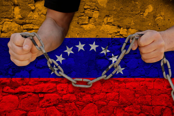 male hands breaking the iron chain, symbol of tyranny, protest against the background of the Venezuela state flag, the concept of political repression, arrest, crime, civil rights, freedom