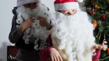 Çocuklar, Noel Baba yardımcıları, beyaz sakallı elfler Noel ağacının yanında neşeyle dans ediyorlar. Yeni yıl konsepti, çocukluk, şenlik havası.