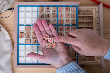 Kadınların ellerini dikkatlice Sudoku bulmacası içine yerleştirirken, meydan okuyan bulmacaları çözmeye kendini kaptırmış yaşlı insanlar, beyin sağlığı, zihinsel aktivite klasik oyunu