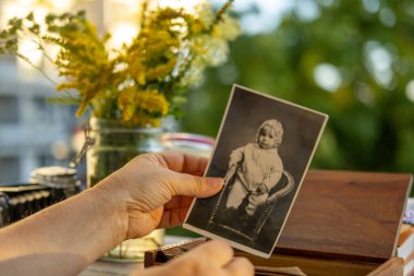 Elleri klasik siyah-beyaz bebek aile arşivi ahşap kutu ve çiçeklerin yanında, nostalji atalarının geçmişinde aile köklerini görüntülerde takip etmek, atalarına yolculuk