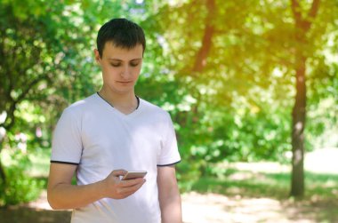 adam park ve ekrana bakarak hareket eden bir smartphone tutuyor. telefon bağımlılığı, sosyal ağlar. Internet üzerinde çalışma. mesajı yazın. Doğa, açık. güneşli bir gün. yakın çekim, metin için yer.
