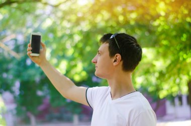 güzel genç Avrupa adam kendini fotoğraflarını ve selfie bir şehir park açık havada yapar. yaşam tarzı, kavram yürür.