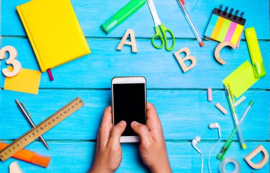 öğrenci okul yönetimi, dijital günlüğü veya e-kitap, isteksizlik öğrenmek için mavi bir arka plan üzerinde okul malzemeleri Smartphone'da tutuyor. eğitim uygulaması. telefon bağımlılığı. üstten görünüm. düz lay