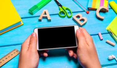 Öğrenci yaratıcı dağınık masaüstü arka planda bir cep telefonu tutuyor. Öğrenci çalışma alanı. Öğrenci ödev yapmak tembel. Eğitim uygulama telefon bağımlılığı